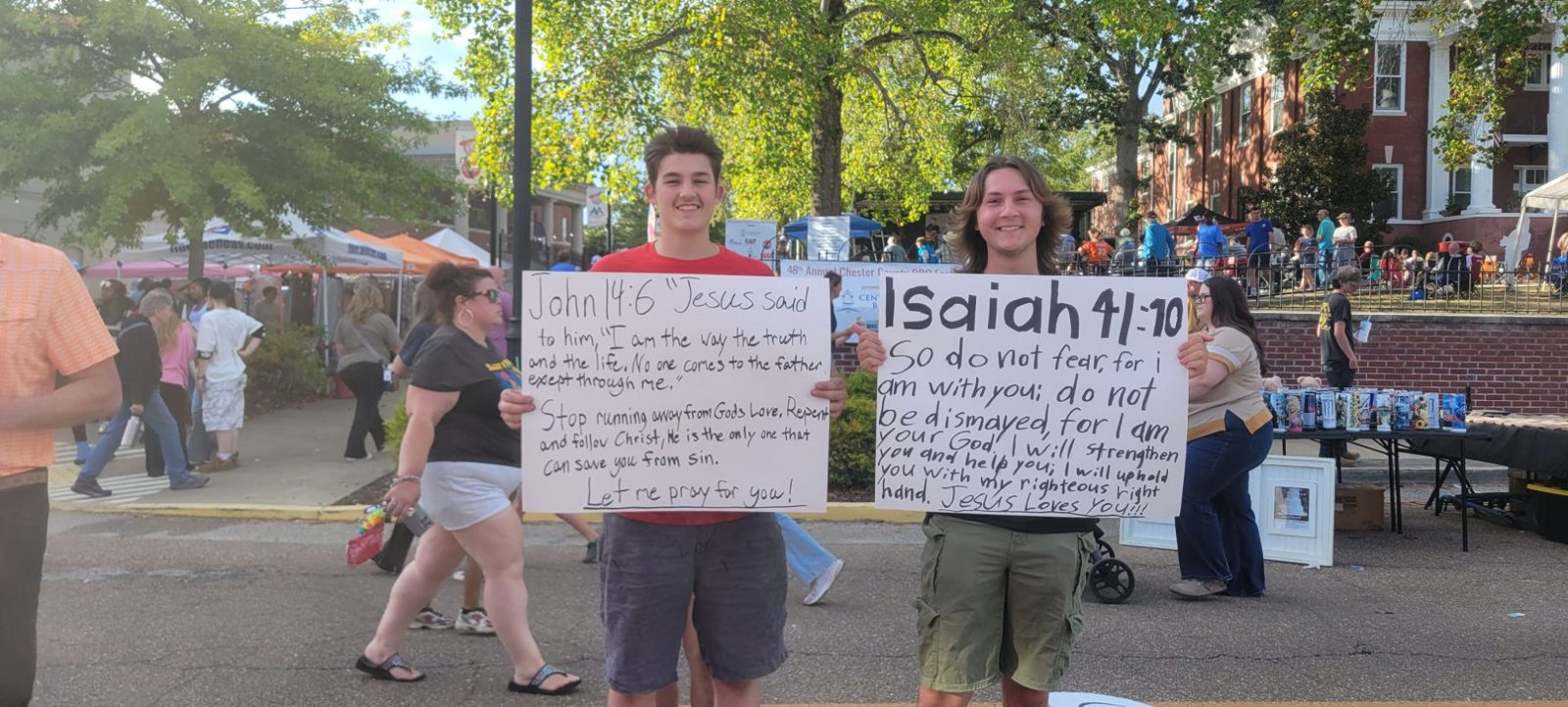 Two young men at the Chester County BBQ Festival holding hand-lettered signs: John 14:6 and Isaiah 41:10